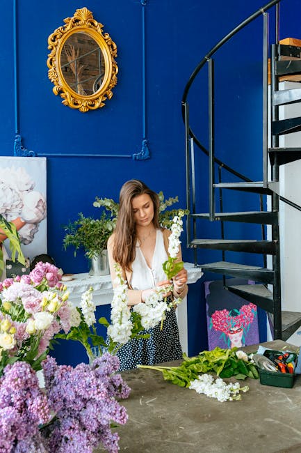 A young woman with long brown hair, dressed in a white blouse and a black-and-white polka dot skirt, is seen arranging a floral bouquet inside a vibrant indoor space. The arrangement includes white an