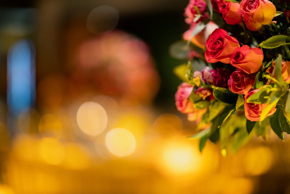A vibrant bouquet of fresh pink and orange roses with lush green leaves, arranged in a tight cluster. The flowers display a variety of rose buds and partially opened blooms, showcasing velvety petals 