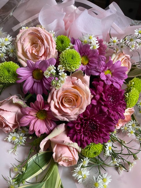 A vibrant floral arrangement featuring light pink roses with tightly layered petals and a soft texture, complemented by bright purple daisies with yellow centers and multiple layers of petals, intersp