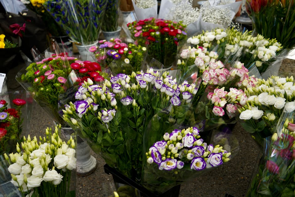 A vibrant display of fresh floral bouquets arranged in clear wrap and placed on a dark stone surface in a flower shop. The bouquets feature a variety of flowers including purple and white lisianthus, 