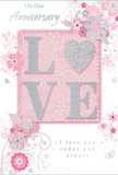 The photograph features a softly romantic anniversary card, its design unfolding with the same gentle intimacy as a quiet walk home through Kennington's tree-lined streets at dusk. The card's focal point is the word LOVE, spelled out in tall, raised letters that have been coated with fine, shimmering glitter. The glitter mixes blush pink and shimmering silver, creating a frosted effect that catches the light, making each letter stand out against the muted background. The letter O subtly echoes the shape of a heart, further deepening the card's message of affection and shared life. Surrounding this central word, an airy scattering of delicate blooms unfurls, illustrated in blush, mauve, and ivory tones softened to almost watercolour transparency. Each petal is traced in graceful, flowing lines, with silver and pale grey details that resemble sunlight brushing over petals in a secluded corner of Kennington Park. Among the floral sprays, you can pick out tiny butterflies, swirling petals, and looping flourishes that add a feeling of movement, like confetti caught in a gentle breeze. The background remains a soft pastel pink, providing a calm, romantic field that lets the flowers and lettering breathe. In tasteful, understated script, the phrases On Our Anniversary and I love you today and always are written in dark, fluid ink that contrasts delicately with the pale tones all around. The overall composition feels like a hushed celebration of a shared journey, elegant and heartfelt without being overly ornate, just the kind of keepsake someone in Kennington might tuck beside a vase of anniversary roses and lilies delivered to mark another year together.